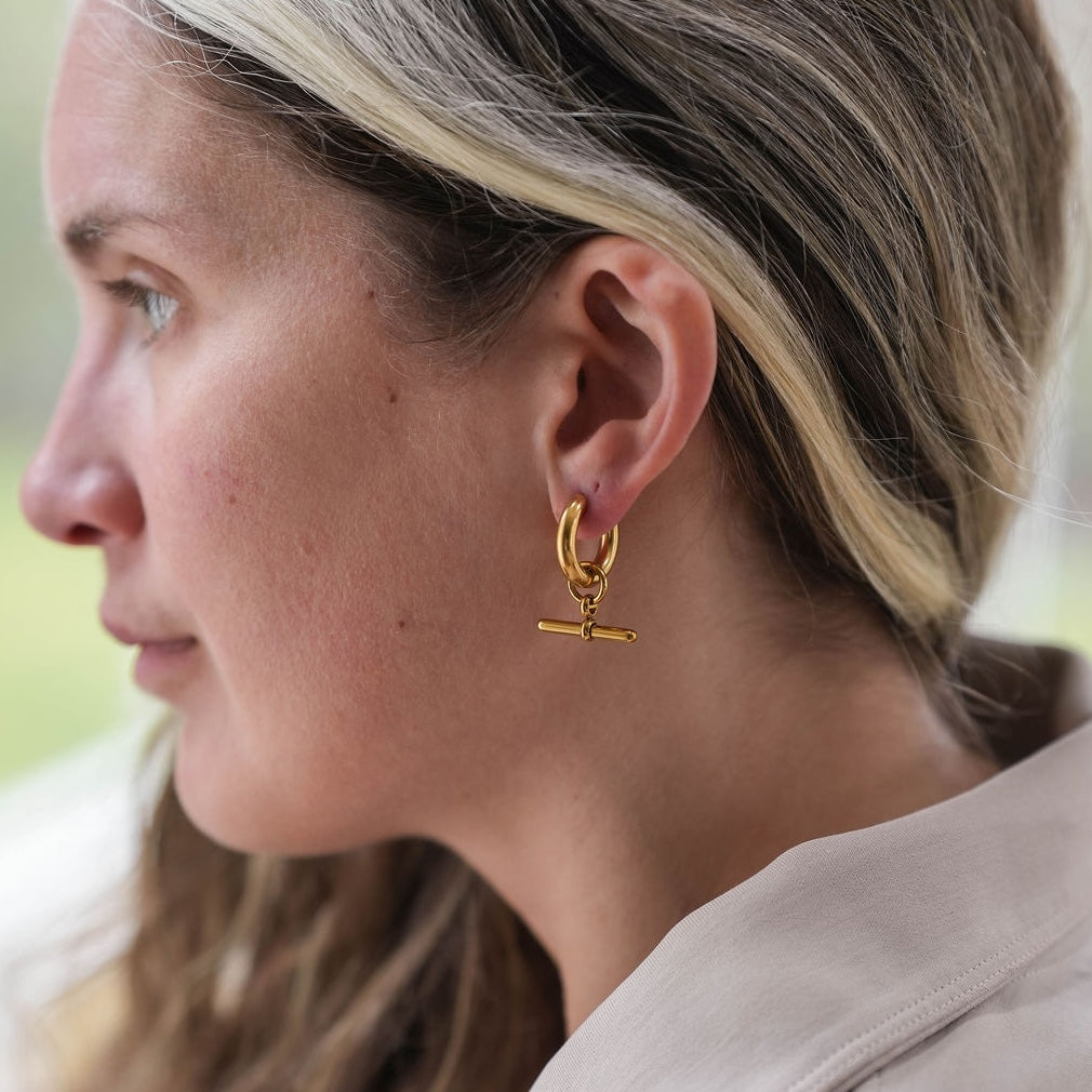 Close-up of a woman wearing a gold earring with a T bar pendant.