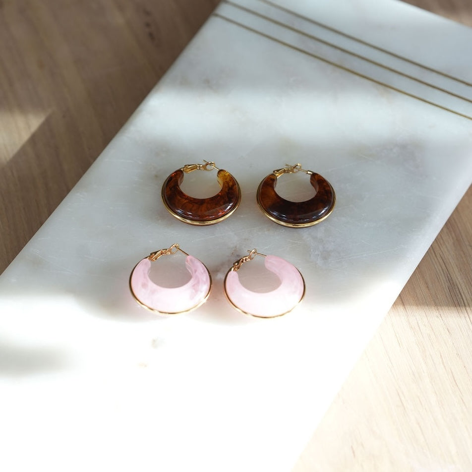 Two pairs of hoop earrings on a marble surface