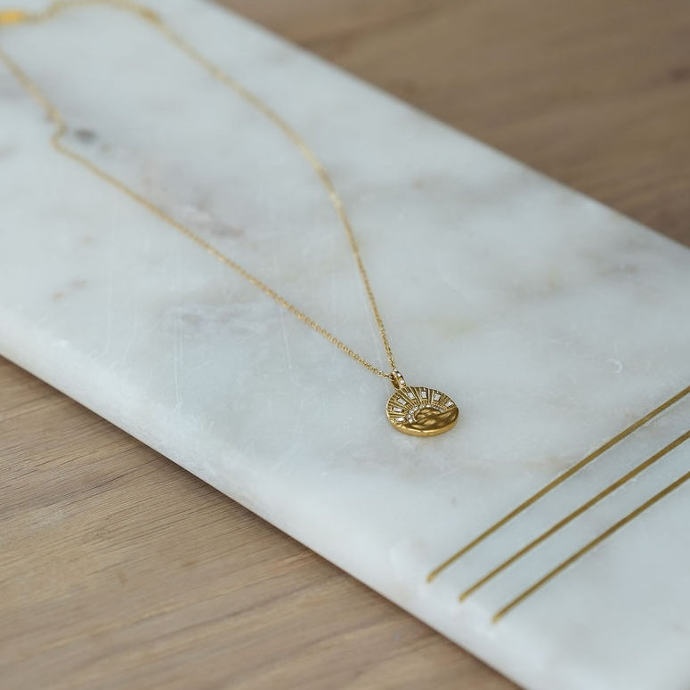 Gold necklace with a pendant on a marble surface