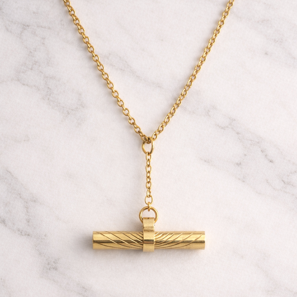 Gold necklace with a cylindrical pendant on a marble background