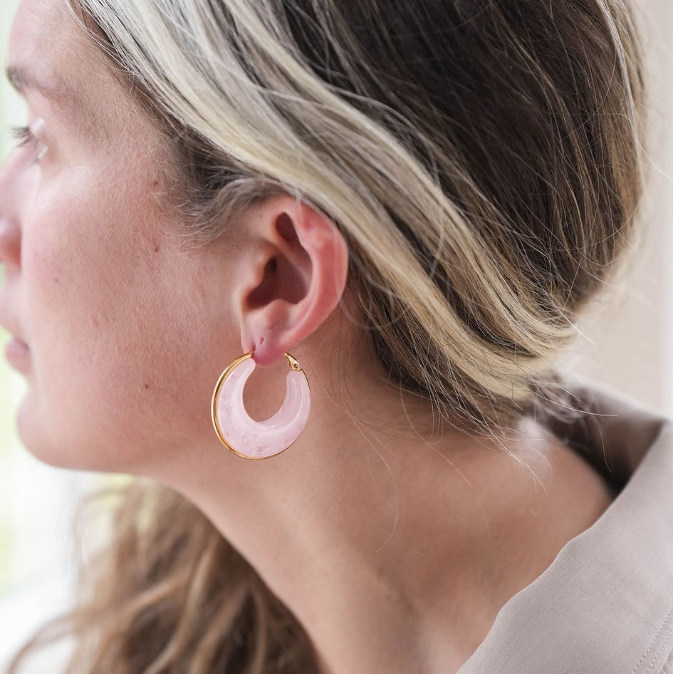 Close-up of a woman wearing pink hoop earrings with gold accents.
