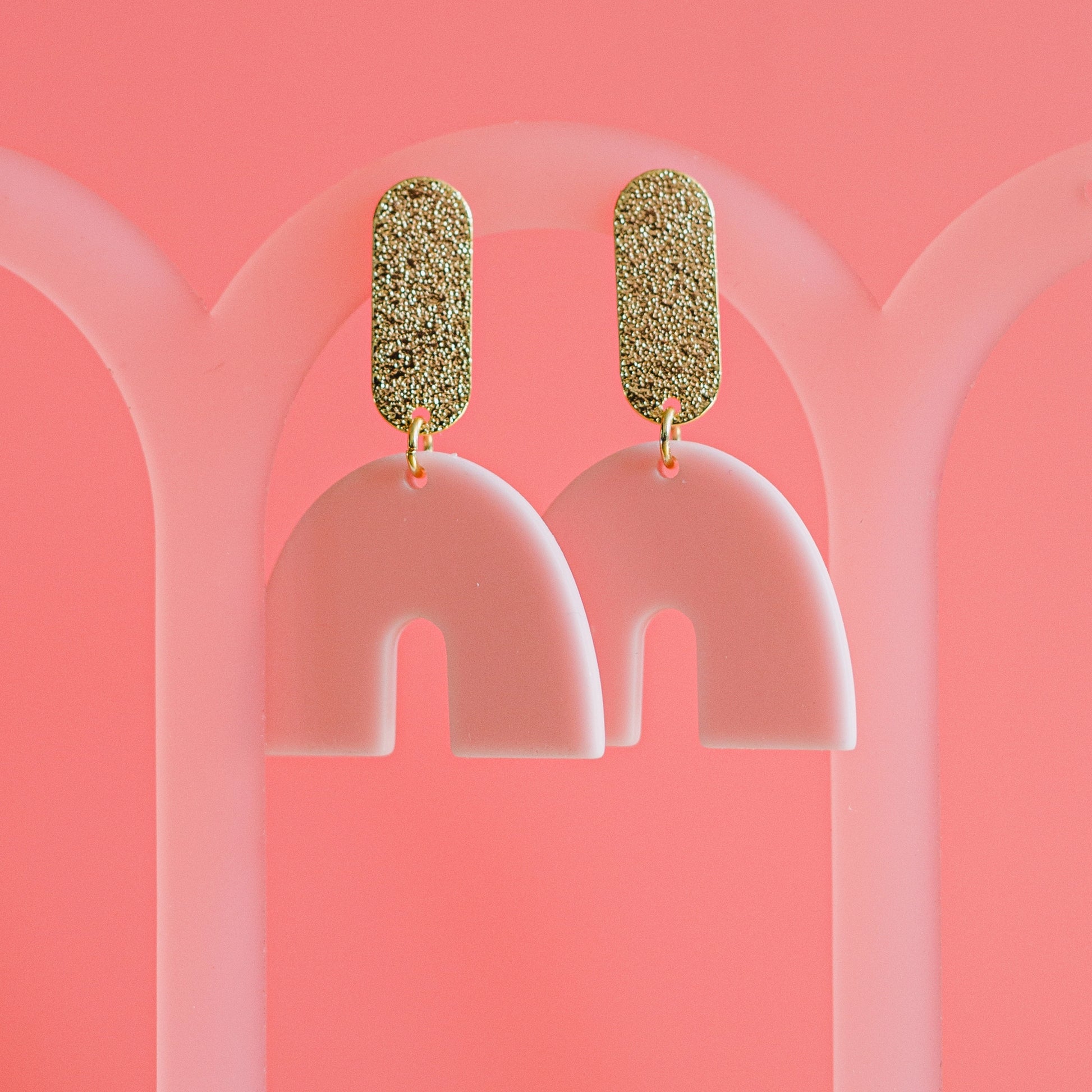 pink arch drop earrings on textured gold bar 